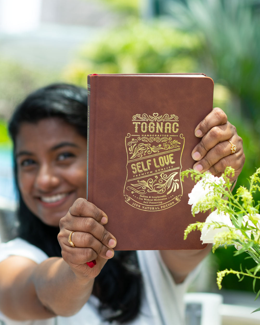 Person holding a brown notebook with 'Self Love' text, outdoors.