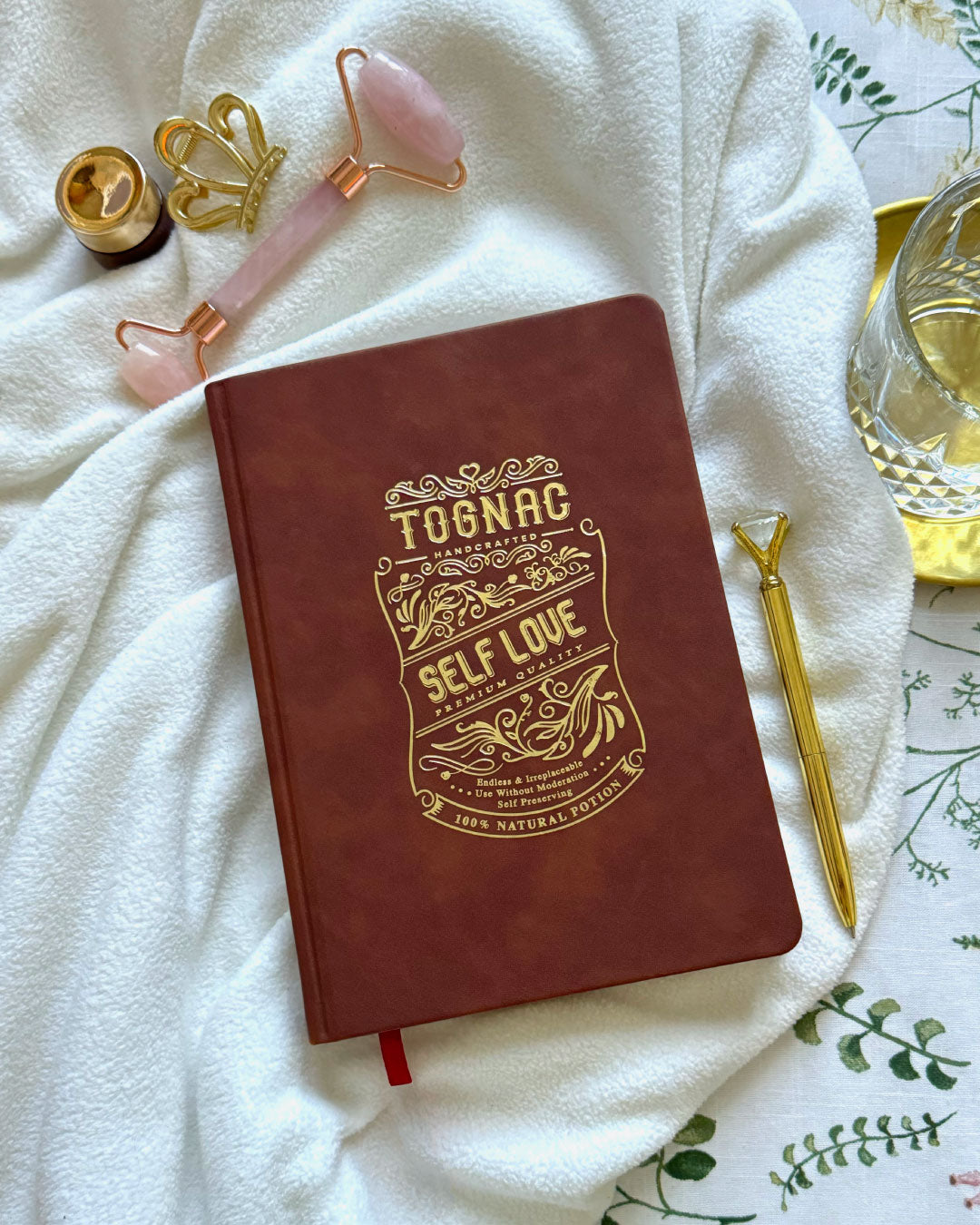 Red notebook with 'Self Love' design on a white surface with wellness tools.