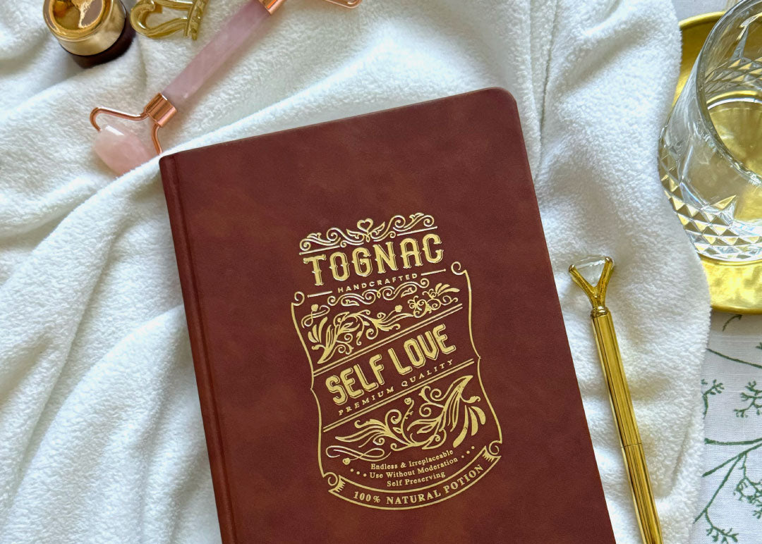 Red notebook with 'Self Love' design on a white surface with wellness tools.