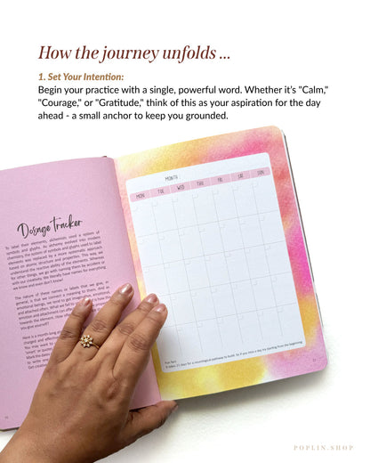Open planner with colourful cover held by a hand on a white background. Set your intentions one ward for the day. 