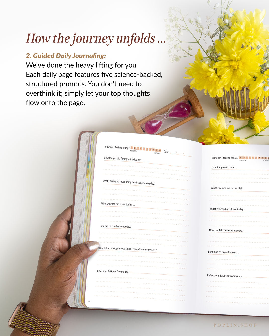 Open journal with daily prompts on a white surface with yellow flowers and an hourglass.